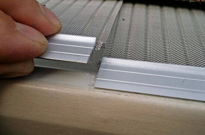 A close-up of a person’s hand installing or adjusting aluminum frame pieces on a mesh screen, featuring stainless steel micro-mesh, possibly for a window or door.