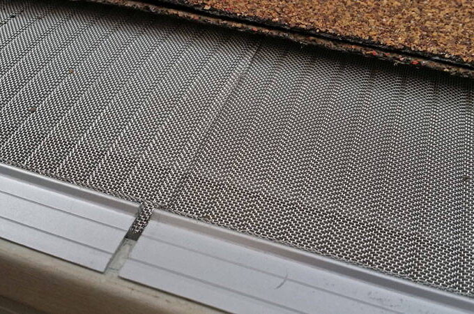 Close-up of a Gutterglove stainless steel micro-mesh gutter guard featuring RiserStep Technology, installed along the roof edge with shingles above, designed to prevent debris from entering the gutter.