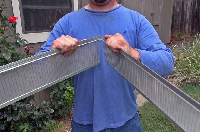 A person in a blue shirt bends two metal studs outdoors near a garden with red flowers and greenery, next to a building with a window—perfect for installing stainless steel micro-mesh or arranging same-day pickup.