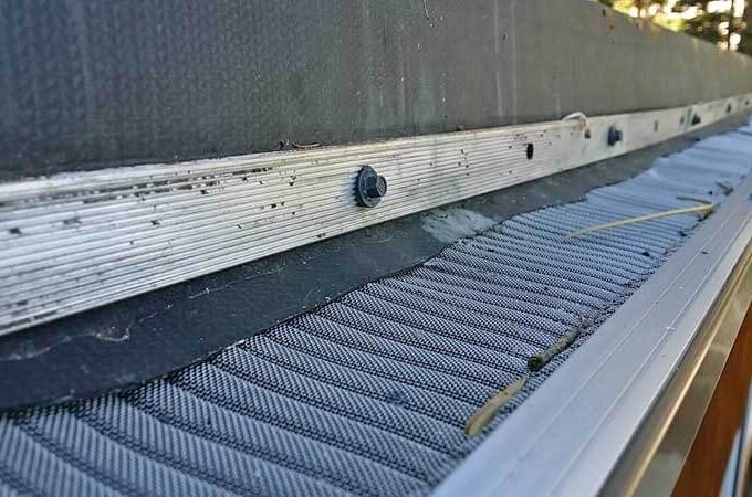 Close-up of a Gutter Guard by Gutterglove with stainless steel micro-mesh attached to the roof edge. Fine mesh prevents debris from entering the gutter, while small twigs and dirt rest on top. Available at Home Depot.
