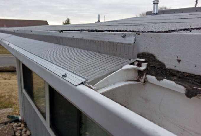 Close-up of a house roof with damaged and cracked fascia and soffit boards, exposing part of the gutter and underlying materials under a cloudy sky—perfect for considering upgrades like stainless steel micro-mesh from Home Depot.