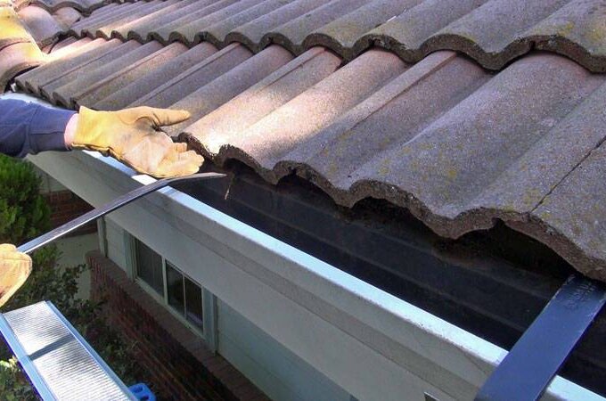 A person wearing gloves uses a crowbar to lift a concrete roof tile near the edge of a house, possibly for maintenance or repair work, with supplies from Home Depot and the convenience of same-day pickup.