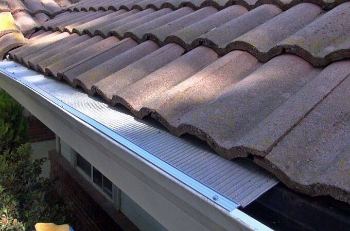 A close-up view of a house roof with brown curved tiles and a stainless steel micro-mesh Gutter Guard by Gutterglove installed over the gutter to prevent debris from entering.