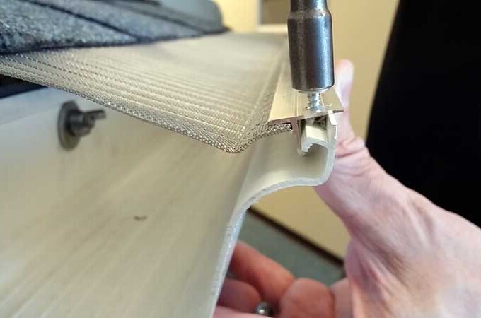 Close-up of a person’s hand installing a screw on the metal edge of a flexible awning or shade fabric using a screwdriver, similar to how Gutterglove's stainless steel micro-mesh is secured for durability and reliability.