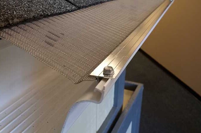 Close-up view of a Gutter Guard by Gutterglove installed along the roof edge, secured with a screw, showing the guard covering the rain gutter to prevent debris from entering; same-day pickup available.